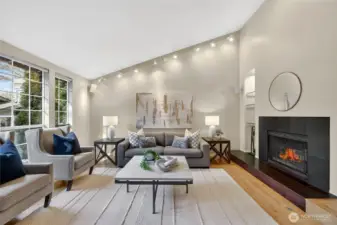 Light-filled living room with soaring ceilings, fireplace & large windows. Stylish finishes, hardwood floors & open layout create a warm, inviting space.