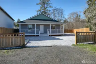 This home features a spacious porch, an inviting exterior, and ample parking on the gravel driveway.