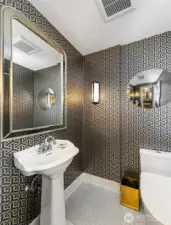 The Powder Room glimmers with quiet drama—its metallic wallcovering, faceted mirror, and sculptural lighting a nod to the mansion’s Art Deco revival. A petite but polished moment of luxury, seamlessly woven into the home’s elegant main floor flow.