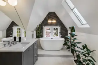 Tucked beneath the gables of the Tower Suite, this En Suite Bath is a spa-like aerie. A freestanding soaking tub rests beneath a skylight and arched stone surround, flanked by greenery and light—an architectural composition of serenity and strength.