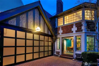 Evening falls on the Auto Court, where the original Tudor silhouette meets modern lines. The trackless glass-paneled garage door hints at the space’s dual life as both Garage and Home Gym, while soft interior glow and leaded glass windows welcome you back to a home of layered elegance.