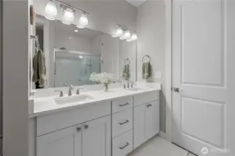 Primary Bath with Dual Sinks – Bright and modern with quartz countertops, sleek fixtures, and a spacious walk-in shower behind glass doors.