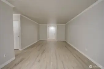 Long open layout for living and dining space - looking to the unit door. Hallway to the left in middle of room. Brand new light colored LVP flooring and freshly painted walls in a neutral tone bring a brightened look to the space. Recessed light installed throughout the ceiling for a clean look.