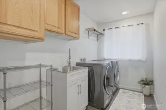 A fully equipped secondary laundry room on the lower level with side-by-side washer and dryer, utility sink and drying rack.