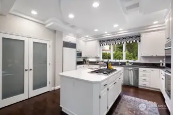 The chef’s kitchen boasts a quartz island with a round veg/prep sink with disposal, Viking 6 burner gas stove, stainless steel microwave, Sub-Zero refrigerator, double ovens, pantry and intricate ceiling details.