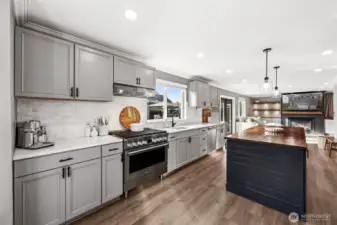 This kitchen shines with stainless steel appliances, large black walnut island, Fridgidaire professional stove, pendant lighting, and quartz countertops with full tile backsplash opening to the family room with cozy gas fireplace & custom built-ins.