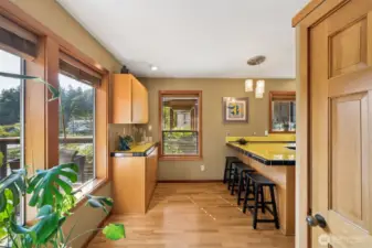 A large, closet pantry to the right, serving bar or baking center, island seating and walls of wood wrap windows atop rich wood floors, invite the cook to create!