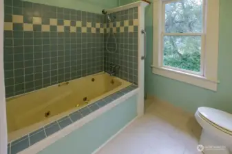 Large main bathroom with jetted tub with beautiful tile surround, pedestal sink, and cozy radiator.