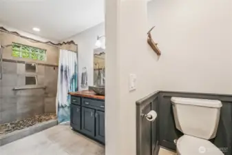 Primary bedroom bathroom features a custom shower and unique stone sink & countertop. Storage is plentiful between the storage closet and cabinet. Radiant heat flooring.