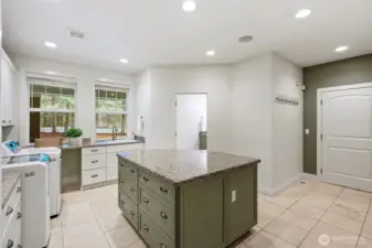 Utility room with granite-topped island for folding and extra storage, utility sink, a full bathroom, and direct access to the 3 car garage and upstairs living space.