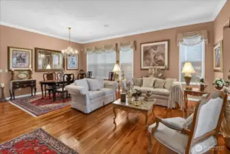 This Grand Living and Dining space is adorned with Crown Moldings, wrapped windows, elegant window treatments, a gas fireplace, classic Chandelier, and warm, custom paint.