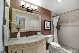The Primary Suite bathroom exudes elegance with its intricately designed vanity, large framed mirror, and rich color palette. Featuring a spacious walk-in shower with stylish tile work, this bathroom offers both luxury and comfort.