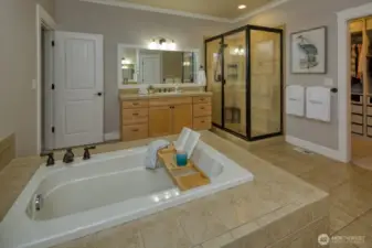 This luxurious primary bath offers a spacious walk-in shower, deep soaking tub, and dual-sink vanity with warm wood cabinetry—all complemented by tile flooring and easy access to the custom walk-in closet.