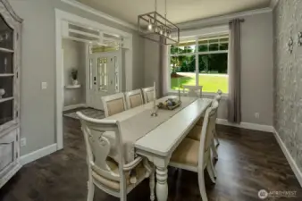 This bright and welcoming dining space opens gracefully to the front entry, showcasing elegant millwork, warm hardwood floors, and a large window that fills the room with natural light and picturesque garden views.