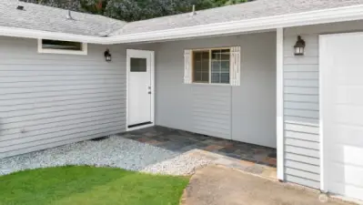 Covered slate tile patio leads to the front entrance. Have you noticed the stone landscaping surrounding the home? Green grass has been digitally altered in photo.