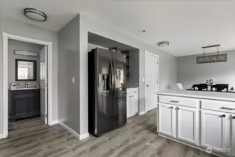 The thoughtfully placed half bath offers convenient access from both the kitchen and living area, while the elegant grey floorboards flow seamlessly throughout the home, adding a touch of sophistication to every room. Door to the right of the fridge is to the garage.