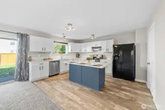 Updated kitchen with white quartz countertops, two-tone cabinets, an island with room for 3 seats, LVP flooring, and a walk-in pantry thru door to the right.