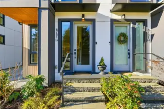 Private front entry with modern glass door, concrete steps, and low-maintenance landscaping.