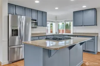 A large eat-up island with cooktop, oven, and stone countertops creates a perfect focal point for the beautiful kitchen.