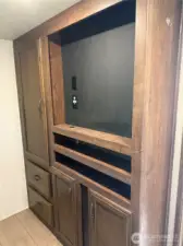 Entertainment center in guest bedroom next to closet and storage drawers.