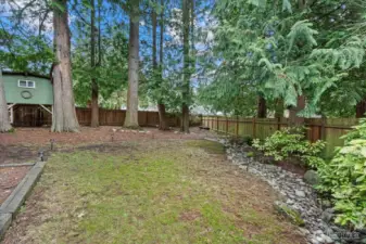 Winter view of the fenced backyard featuring a grassy area for relaxation, a side garden, and a playhouse.