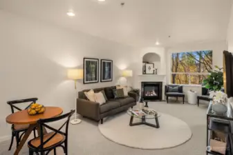 Spacious living room with gas fireplace, slider to private balcony, and oversized window with green outlook.