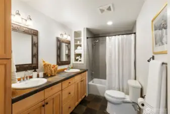 Beautifully refreshed bathroom with double sink vanity, tile shower, slate floors, and fun, whimsical fixtures.
