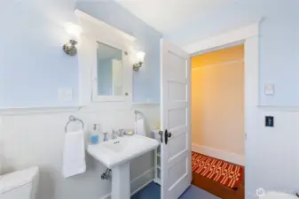 There are push-button switches and a storage cabinet behind the door.  You can see the hallway through the door.  To the left of the bathroom door at the end is the Bedroom.