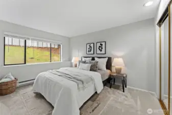 Serene bedroom featuring plush carpet, soft neutral tones, and a large window that fills the room with natural light. Generously sized with space for a king bed, mirrored closet doors, and a peaceful outlook—an ideal retreat at the end of the day.