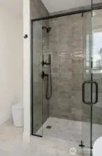 The primary shower features floor-to-ceiling custom tilework, and dual-nozzle hardware.