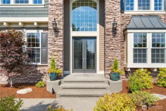 Grand double-door entry framed by stonework, planters, and elegant exterior lighting creates a warm, upscale welcome.