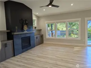 Open floor plan. Built-in cabinets and shelves, stacked stone propane fireplace, modern ceiling fan, luxury vinyl plank flooring