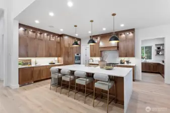 Gourmet kitchen showcasing a 48” Wolf range top, built-in refrigerator and appliances seamlessly integrated with custom cabinetry. A waterfall-edge quartz island anchors the space, complemented by designer cabinetry, statement pendant lighting, and a stylish wet bar with bar sink—perfect for entertaining.