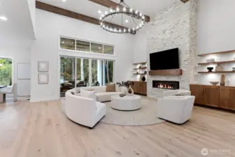 Impressive great room with soaring 20’ ceilings and a grand sense of volume. A custom gas fireplace with a striking stone surround anchors the space, framed by bespoke cabinetry and illuminated shelving with integrated low-voltage lighting—creating warmth, sophistication, and style.
