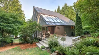 Enjoy this striking architectural design and low-maintenance metal roof surrounded by lush greenery, complete with a spacious deck for outdoor living.