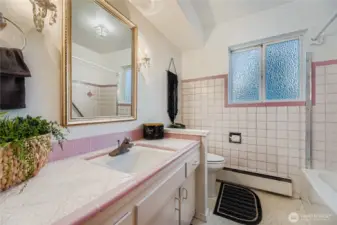 Retro-chic full bath with vintage pink tile, spacious vanity, and natural light from the window.