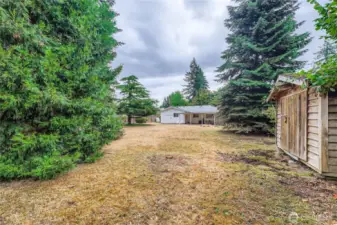 Deep backyard with open lawn space, mature trees, and room for gardening, play, or future projects