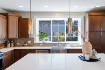 Chef-inspired kitchen with quartz countertops, a generous island, designer pendants, stainless steel appliances, rich cabinetry and a large window.