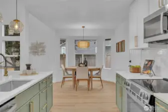 The chef's kitchen features on-trend sage green cabinetry with gold hardware and flows effortlessly into a sunny dining nook surrounded by windows. Multiple windows and thoughtful lighting create a bright, airy space perfect for both daily meals and entertaining.