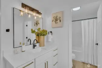 The primary en-suite bathroom features dual vanities with brass hardware, black fixtures, and a skylight that brightens the space.