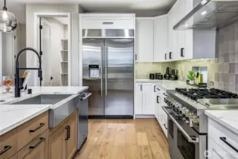 A chef-inspired kitchen anchored by a premium JennAir refrigerator and a 48-inch professional gas range. Expansive quartz surfaces, a deep stainless farmhouse sink, and curated pendant lighting combine to create a workspace that is both functional and beautifully designed. The walk-in pantry just beyond the refrigerator offers exceptional storage and organization.