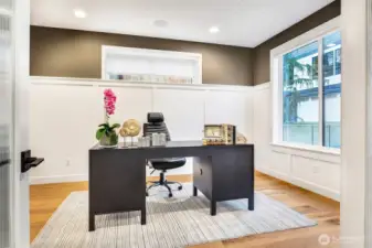 A bright and inviting main-level office framed with elevated millwork, warm wood flooring, and a chic two-tone palette. Oversized windows bring in natural light, creating an ideal setting for productivity, creativity, or quiet work-from-home days.