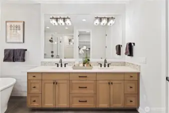 The primary bath features a large double vanity with rich wood cabinetry, quartz countertops, and a full-width mirror illuminated by modern crystal-accent lighting.