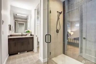 A beautifully appointed ensuite bath featuring a wide vanity, quartz counters, and striking matte-black fixtures. The oversized frameless glass shower showcases dimensional designer tile for a clean, modern finish, while thoughtful layout provides privacy and ease of use for adjacent bedroom with direct ensuite access.