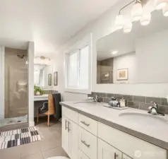 The gleaming interiors of this primary ensuite are very complimentary of the beautiful primary bedroom. This space features a double vanity with full-length mirror and step-in shower with handheld fixtures. Don't miss the brilliant seated vanity space seen here.