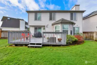 View of the back of the house. Easy care landscaping. Greenery borders the deck area.