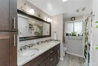 Spacious updated hall full bathroom with dual sinks, durable quartz counters, and an overhead skylight.