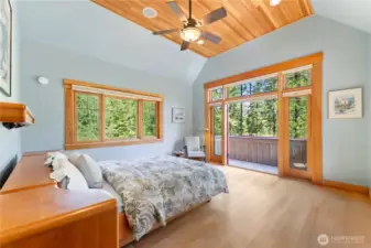 Vaulted wood ceiling, private balcony, and large windows bring light, warmth, and forest views into the luxurious primary suite.