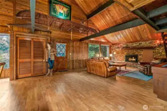 Vaulted cedar ceilings and dark beams draw your eyes up, while hardwood floors ground the space in rustic warmth. A massive brick fireplace wall anchors it all. Quirky details make it unforgettable: a shingled-roof coat closet, a wooden canoe perched above, Native American artwork filtering the light, and yes—Madeline the mannequin keeps her watch from the wall, ready to stay with the house.