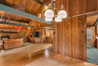 The dining room can’t help showing off—peek left and the fireplace steals the scene, glance right and the kitchen waves you in. Overhead, beams stretch like arms connecting it all, giving the whole lodge that one-big-room kind of feel.